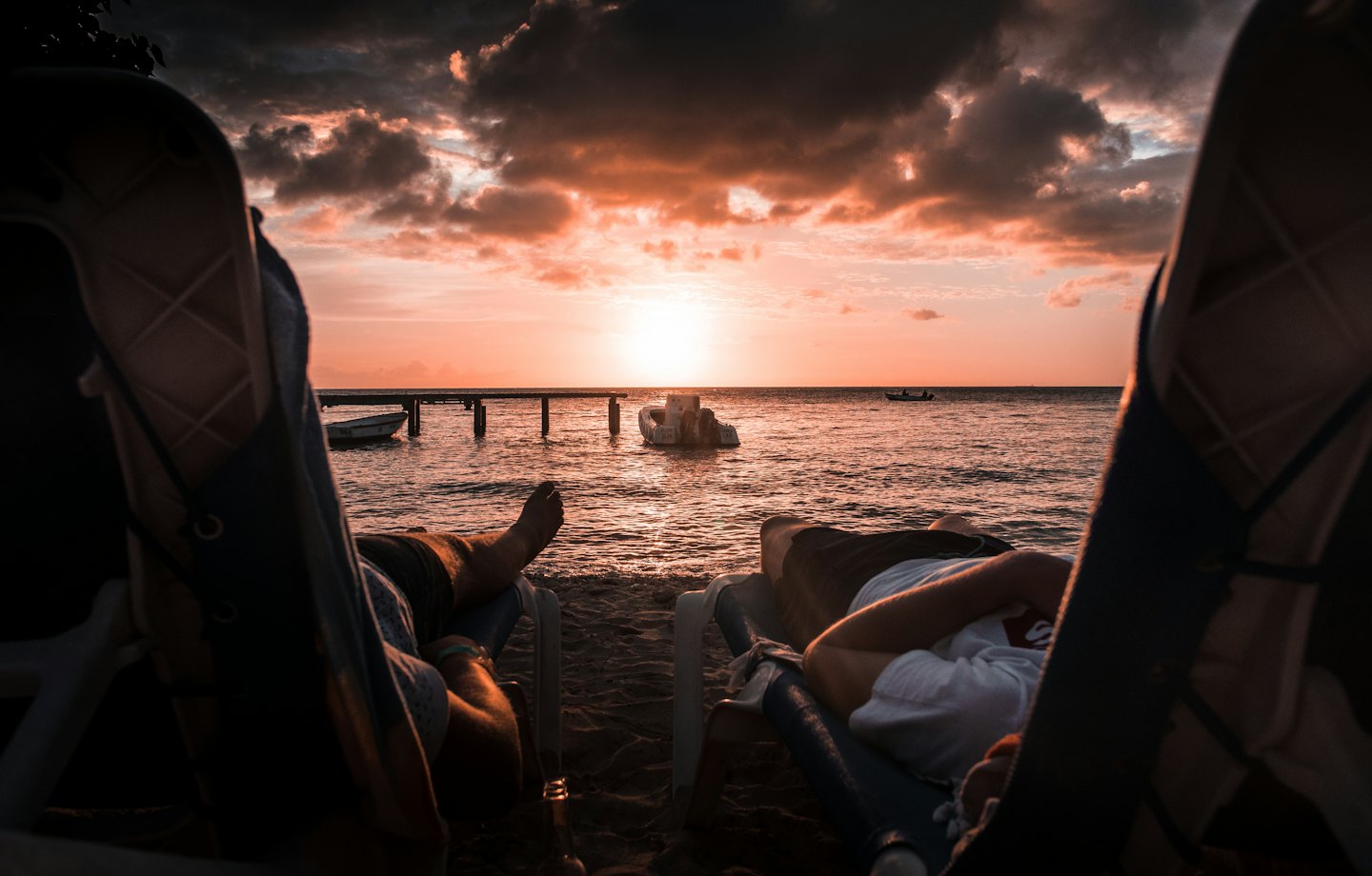 Two people relax in beach chairs watching a sunset over the ocean.