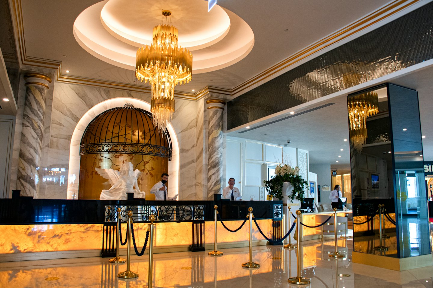 Two men behind a hotel reception desk with gold accents.