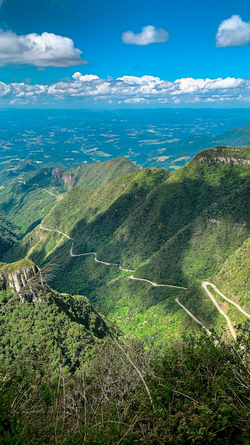A winding road cuts through forested mountains on a clear day.