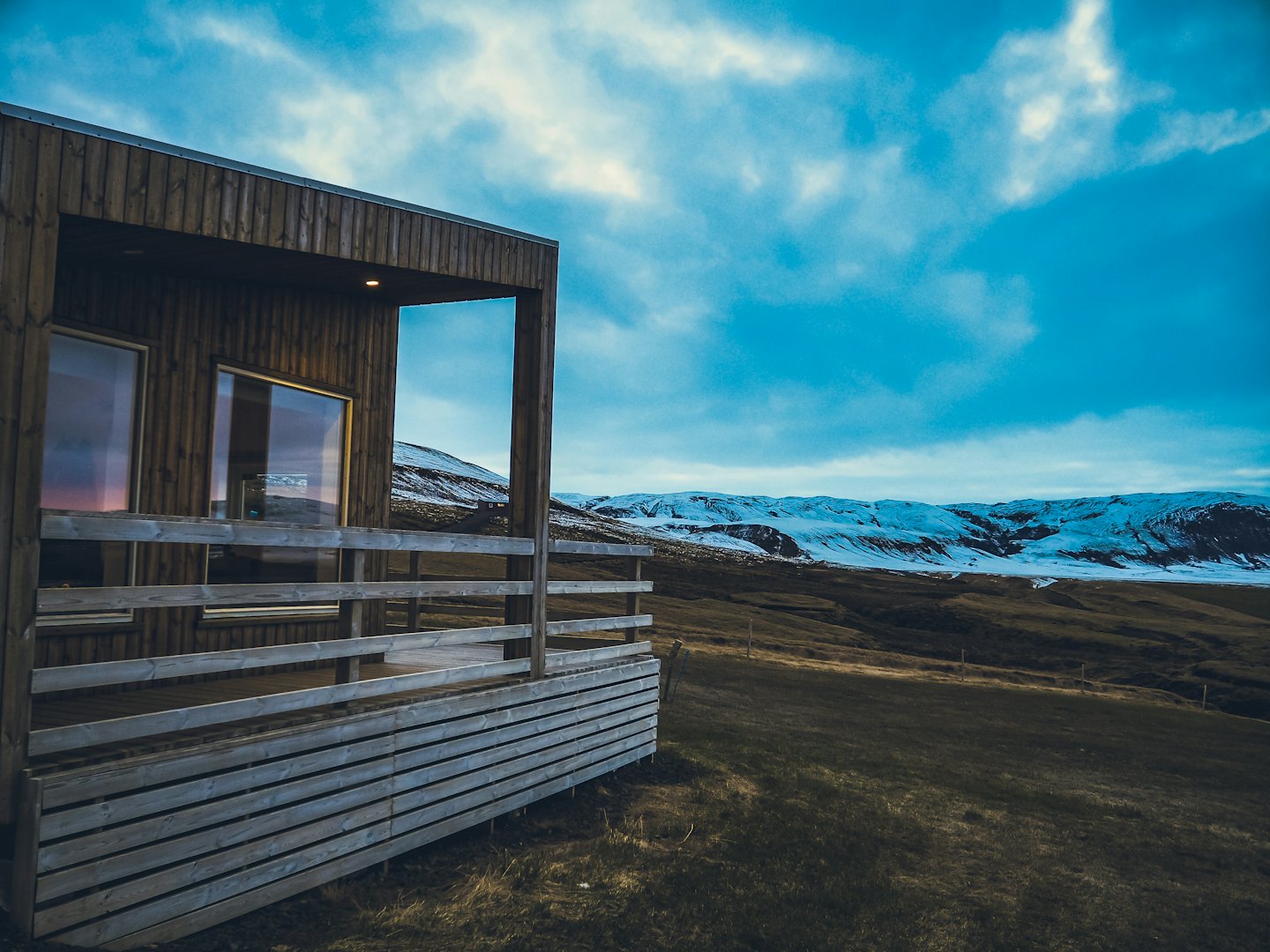 Modern wooden cabin with a deck sits on a grassy hill.