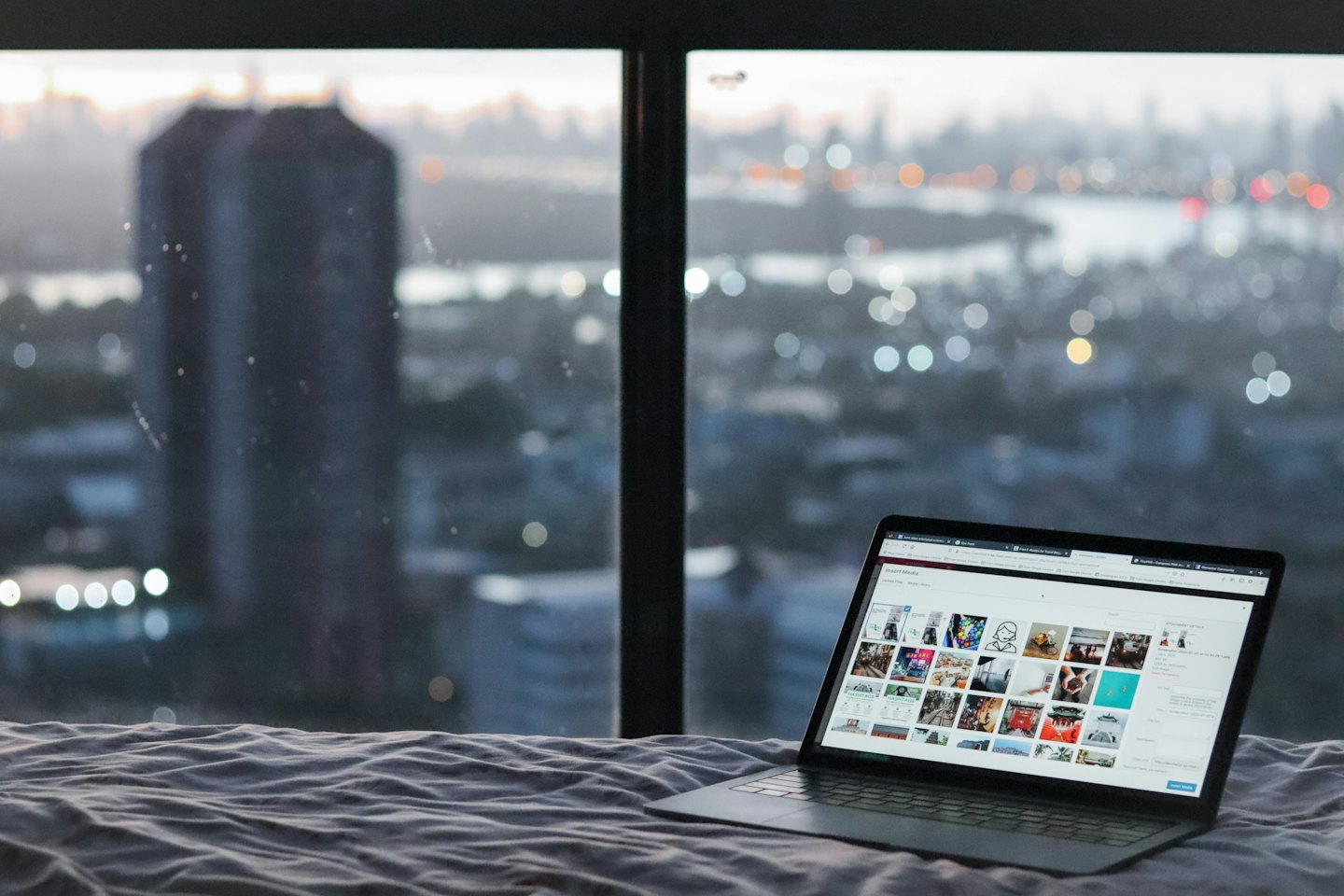 Laptop displaying stock photos on a bed near a city skyline.