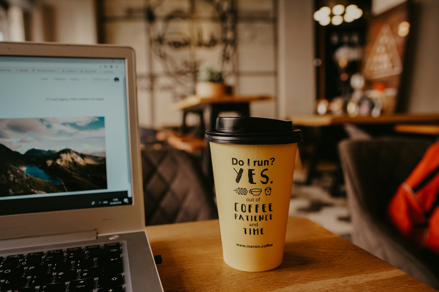 Laptop displaying a mountain scene next to a coffee cup on a wooden table.