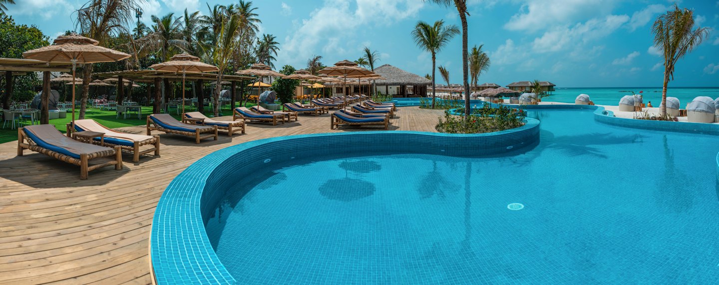 Tropical resort pool deck with palm trees and ocean views.