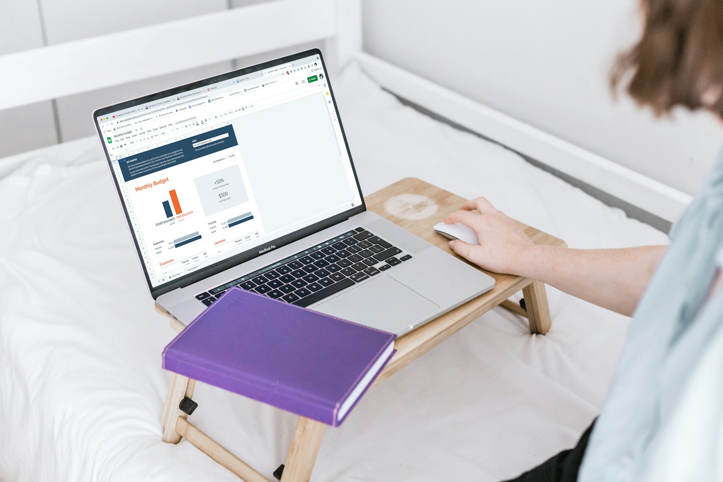 Person working on a laptop with financial spreadsheet on a bed.